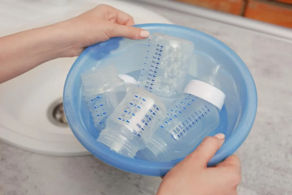 Parent washing PP baby bottles in a blue basin before sterilising them
