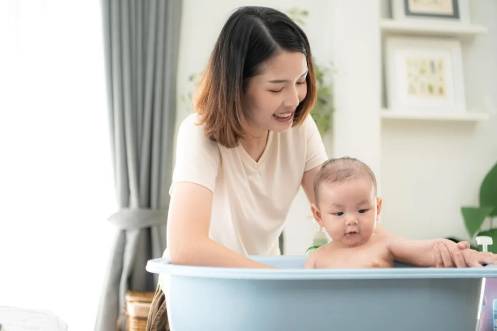 Mother gently bathing her baby in a bathtub at home as part of a calm and caring newborn bath routine.